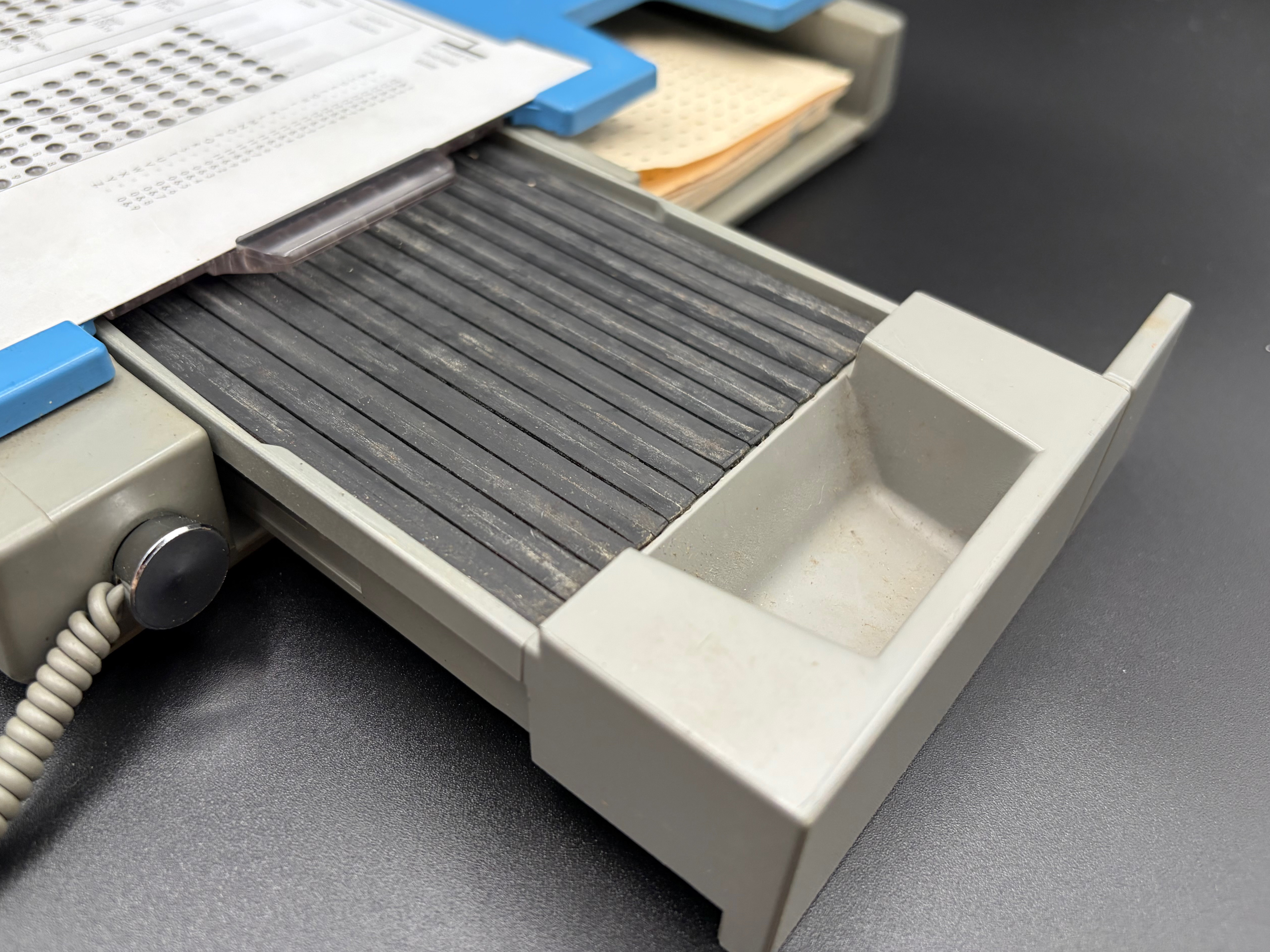 Detail of the open sliding drawer where the perforated card is inserted for punching. No card is inserted, showing the plastic underneath which captures punched chads.