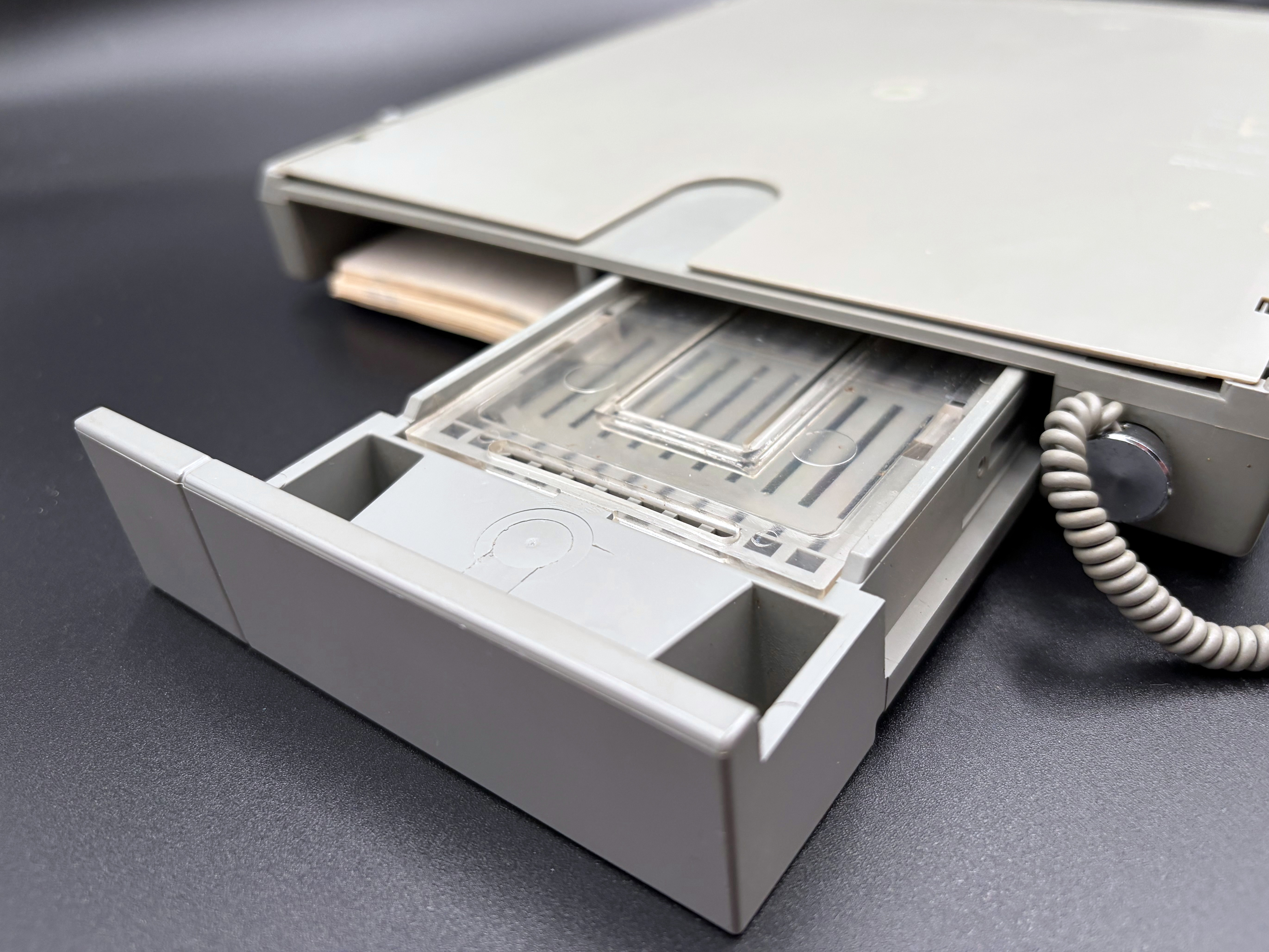 Detail of the rear of the open sliding drawer. A transparent plastic piece is shown which holds punched chads.